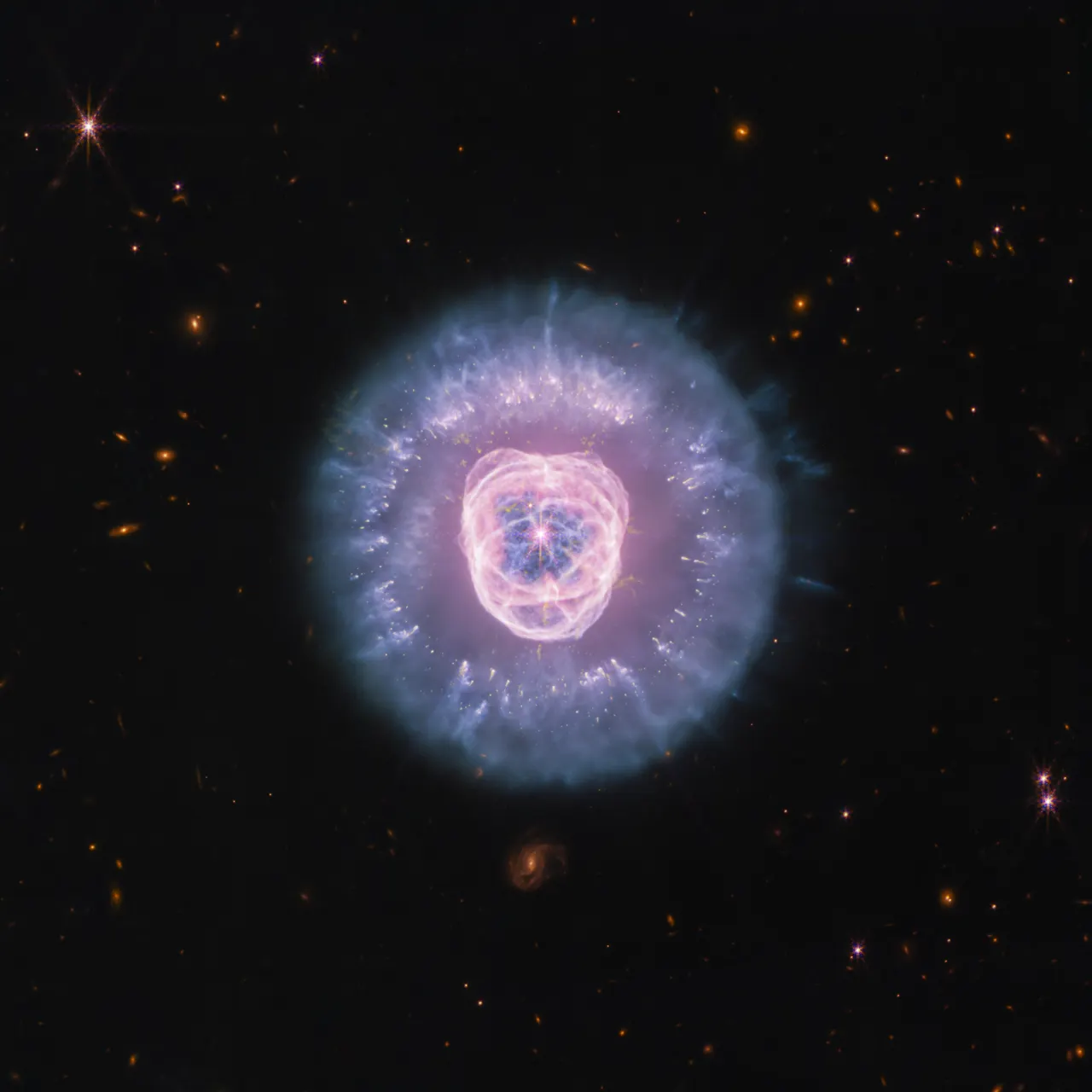 JWST’s Near Infrared Camera and Mid Infrared Instrument combined image of planetary nebula NGC 2392, the Lion Nebula, against the black background of space. The nebula is at center, circular in shape,