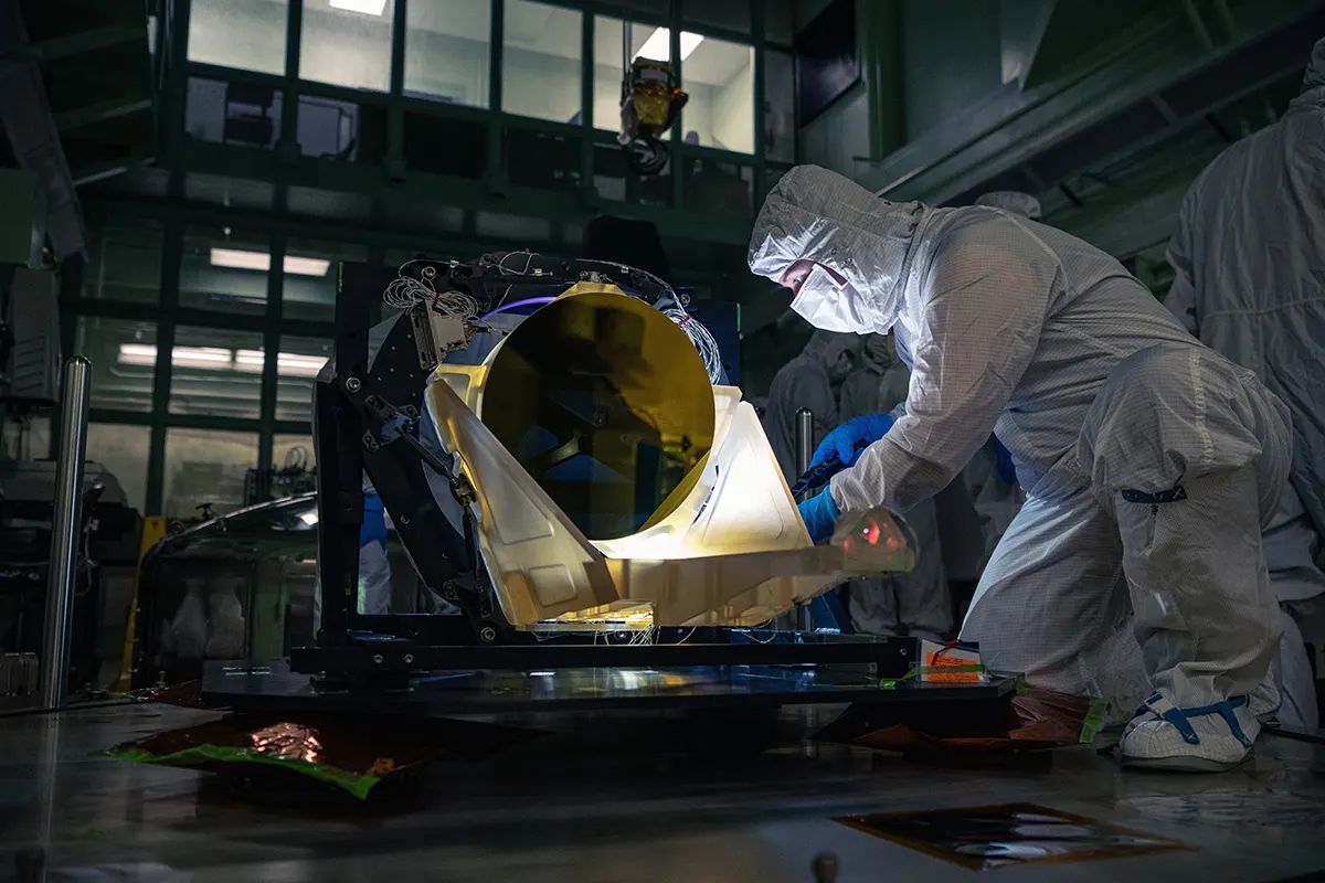 The prototype LISA telescope undergoes post-delivery inspection in a darkened NASA Goddard clean room on May 20. The entire telescope is made from an amber-colored glass-ceramic that resists changes in shape over a wide temperature range, and the