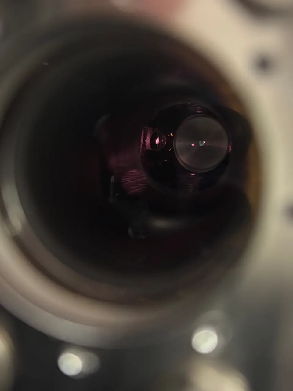 View through a circular opening into a dark interior. A red dot floats in the darkness.