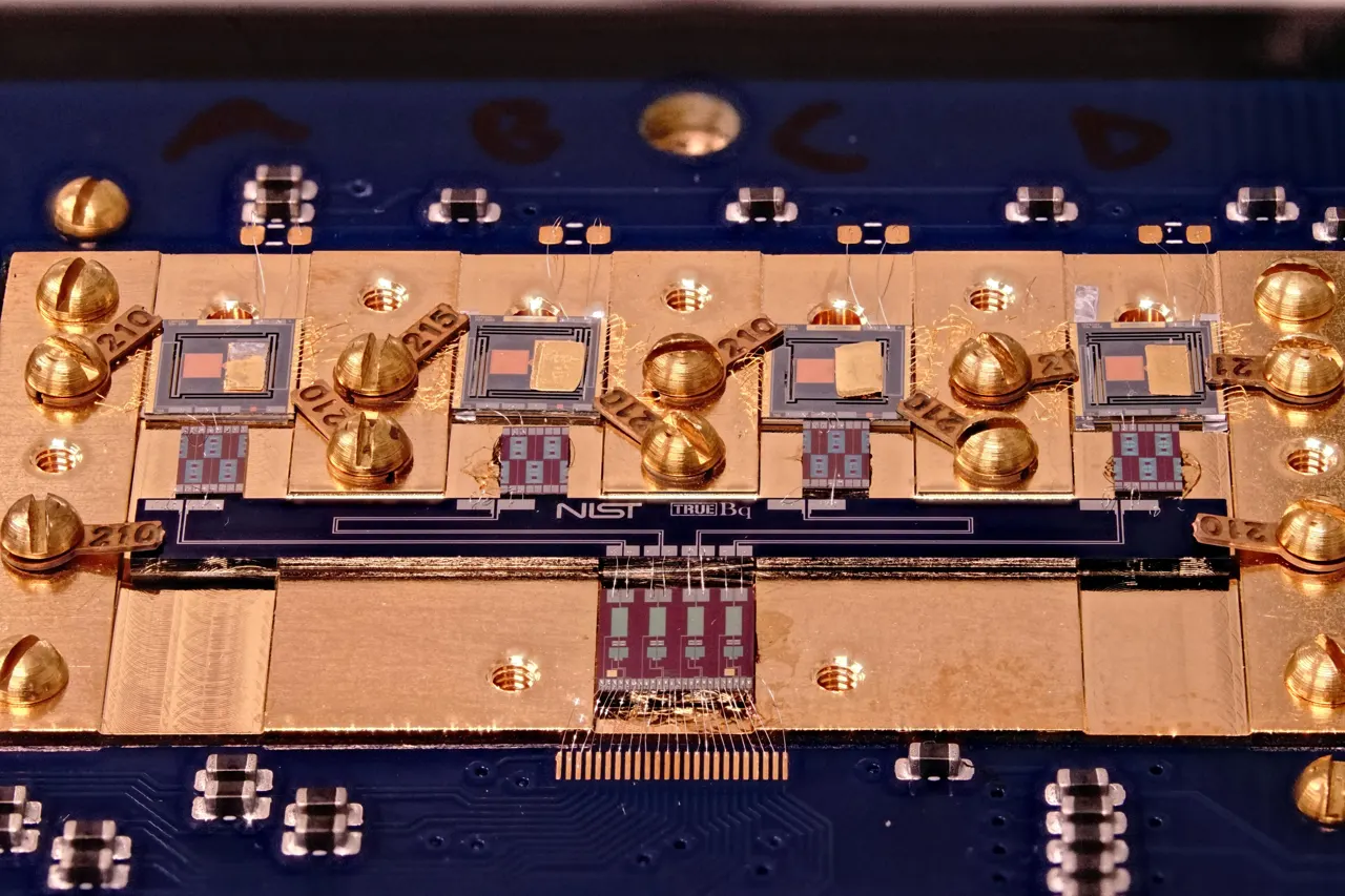 Circuit board with various square chips and gold screws. Small letters in the center say: NIST True Bq.